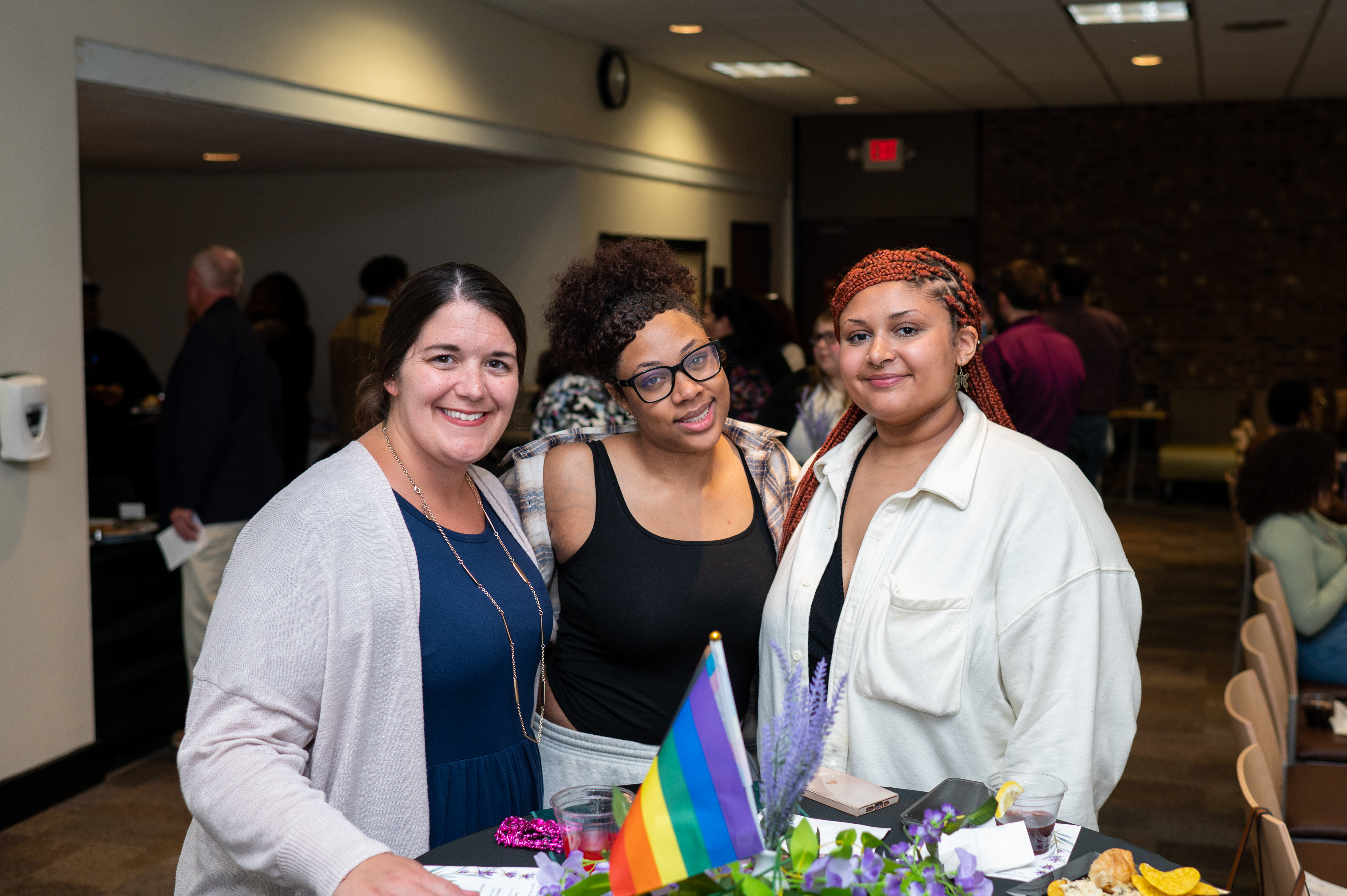 Three guests standing in front of a bistro table decorated with lavender and a pride flag