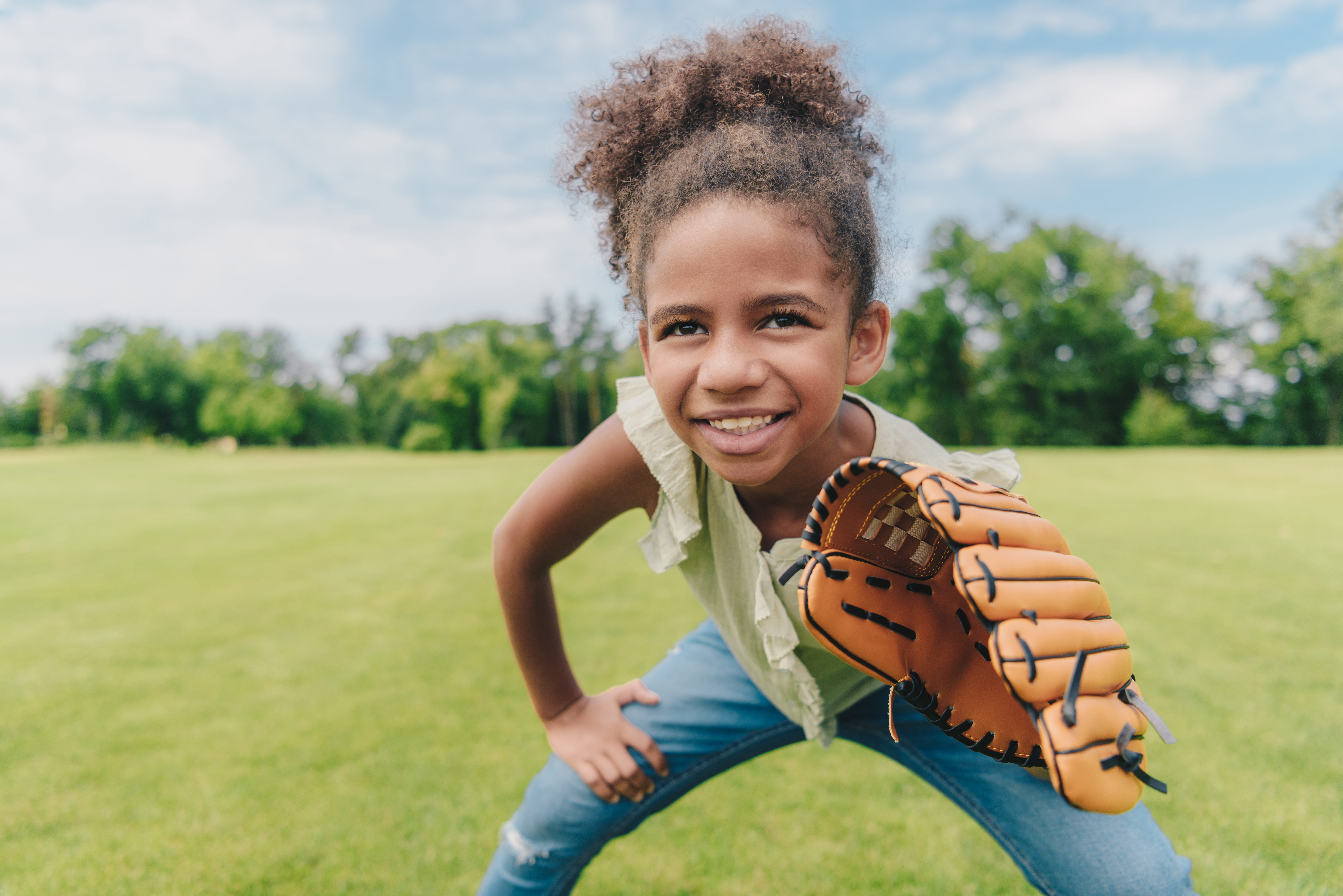 Adolescent girl holding a softball mitt playing in a field