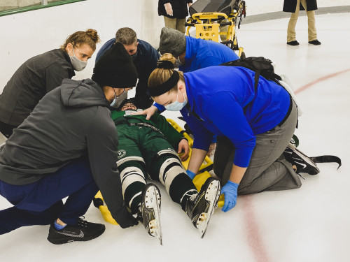 Athletic Training staff helping hockey player laying on the ice