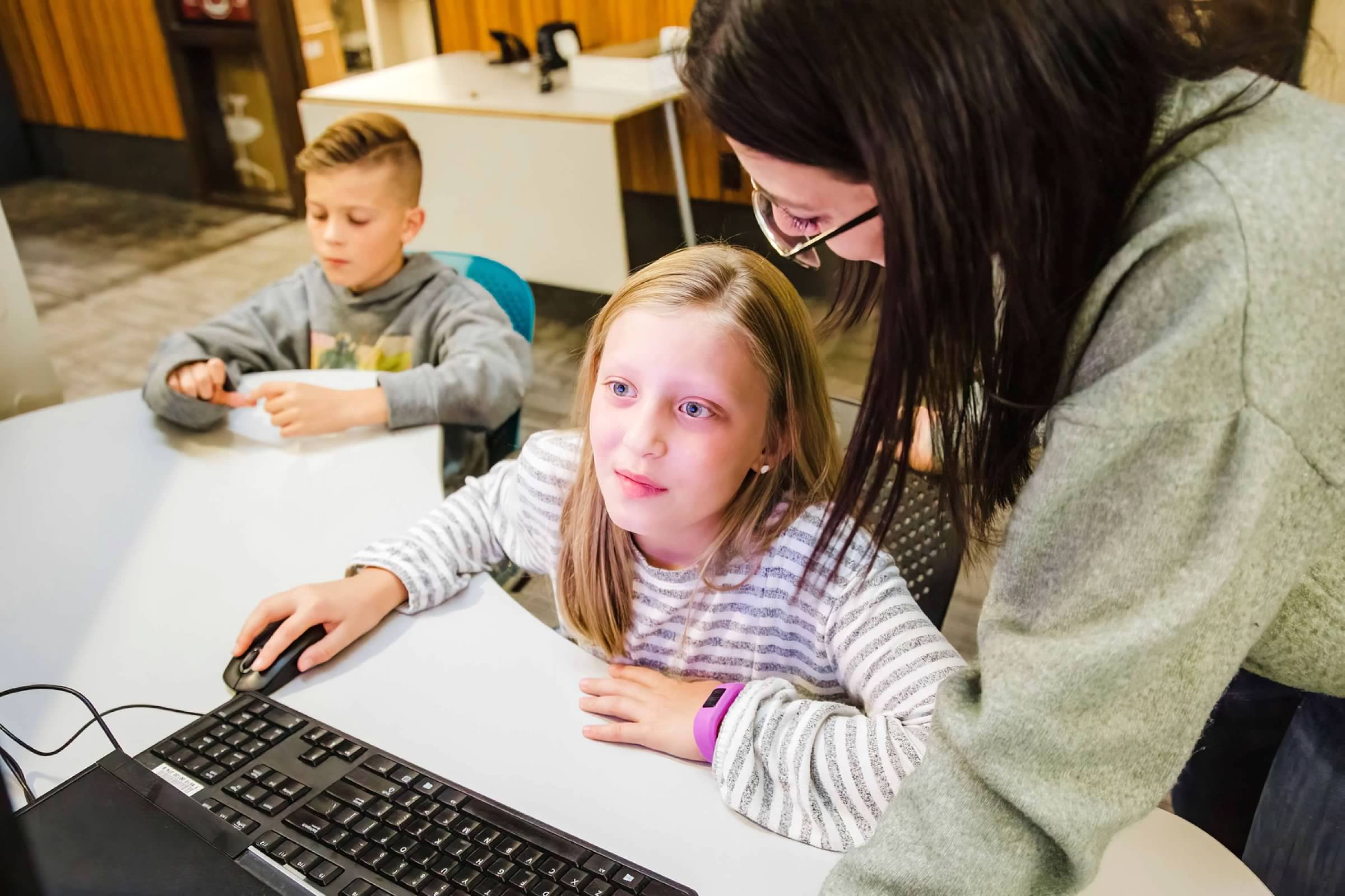boy and girl working on computer with teacher