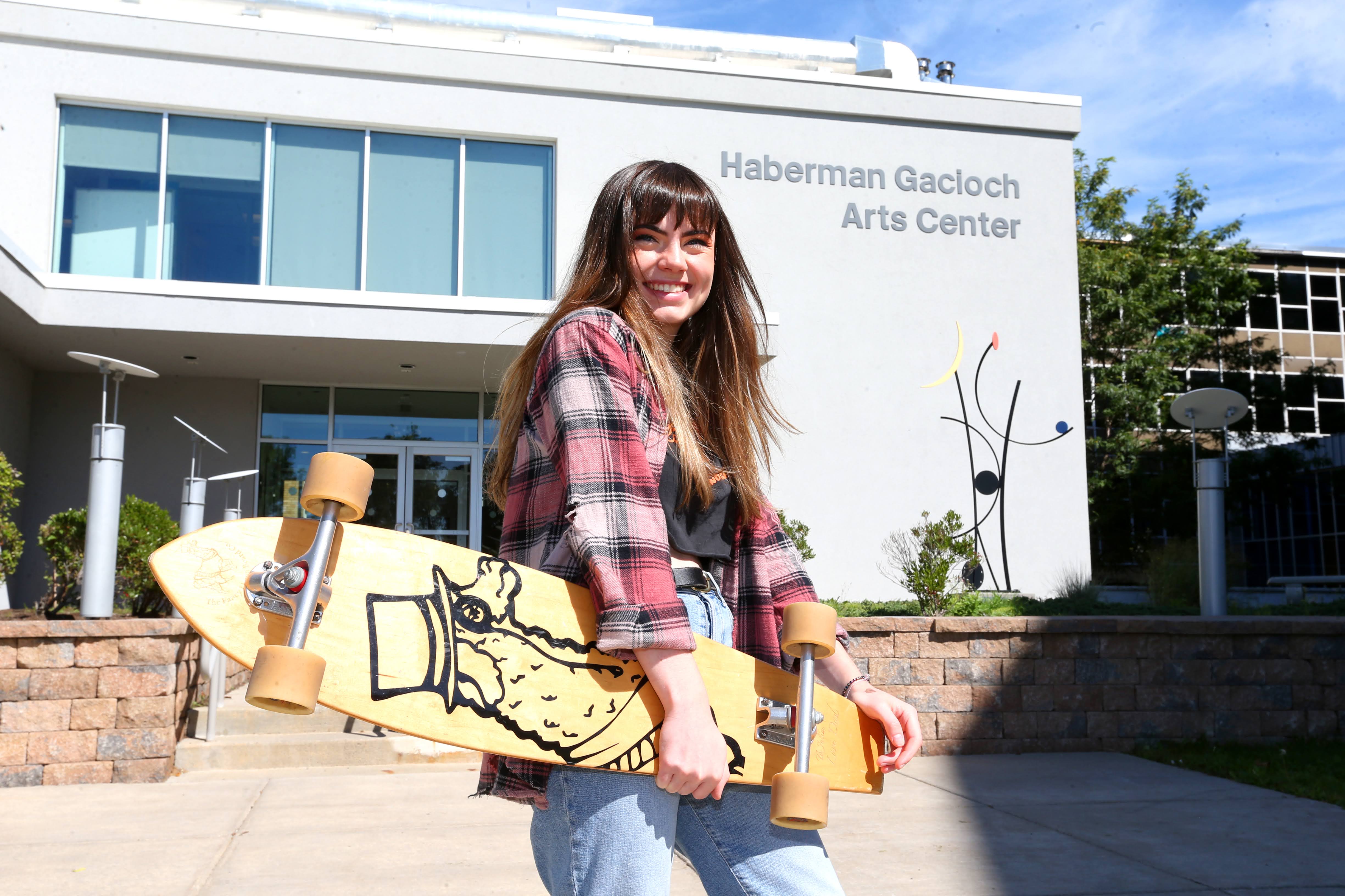 Exterior of Visual and Performing Arts Center; female student holding a skateboard