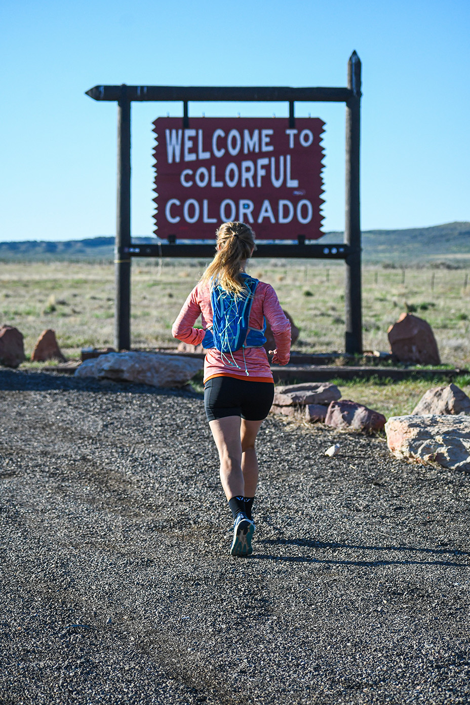 Meghan Guhler ‘16 running with back to the camera sign in front of her that says Welcome to Colorado