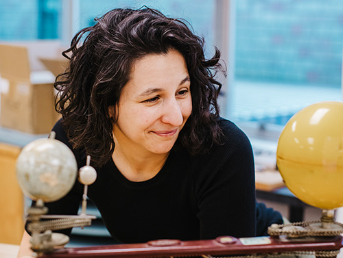 Dr. Hannah Attard leaning on table galaxy model in front of her