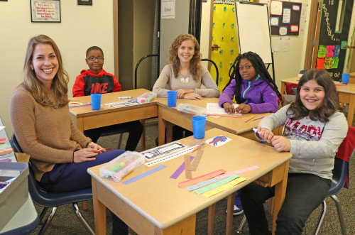 Teachers sitting at desk helping grade school children