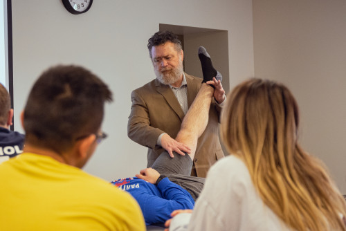 PT Chair Michael Ross working on a students elevated leg in a classroom