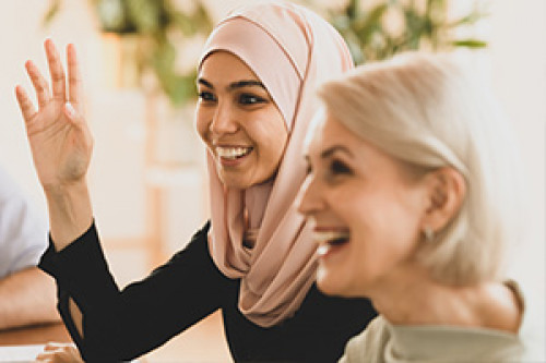 Woman wearing a hijab smiling and raising her hand