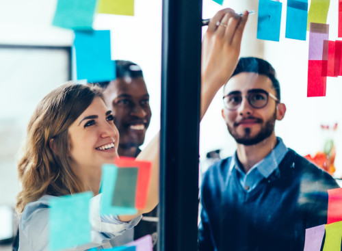 Office workers collaborating on a project using post-it notes on a glass wall.