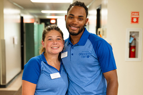 Male and female student in blue orientation staff polos standing in Duns Scotus hallway
